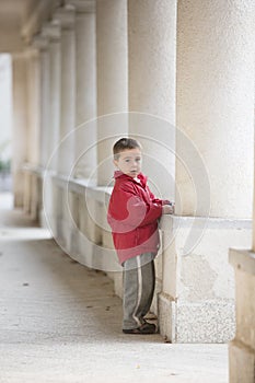 Young boy stands next to white columns