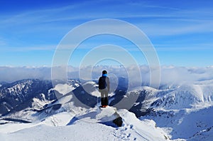 Young boy stands on peak of Chopok mountain and below it lies the Demanovska valley and in far High Tatras. Fairy-tale panorama