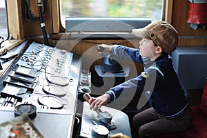 A young boy steering a locomotive and train in a driving compartment or cabin with handles and meters as a train driver