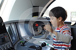 A young boy steering a locomotive and train in a driving compartment or cabin with handles and meters as a train driver