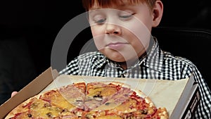 A young boy with a strong desire looks at the pizza. A hungry child really wants to eat a piece of pizza. Dark background. Red-