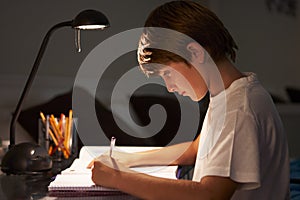 Young Boy Studying At Desk In Bedroom In Evening