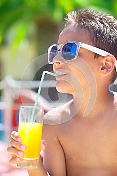 Young boy with sunglasses on beach enjoys and drinking juice