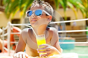 Young boy with sunglasses on beach enjoys and holding juice