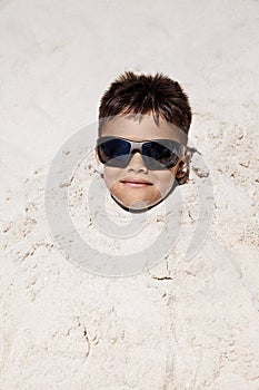 Young Boy In Sunglasses Buried In The Sand At The Beach