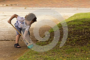 Young boy sweeping leaves from the driveway