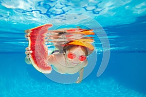 Young boy swim and dive underwater, hold watermelon. Under water portrait in swim pool. Child boy diving into a swimming