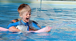 Young boy in the swimming pool with a rubber ring and a water spout.