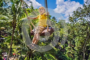 Young boy swinging in the jungle rainforest of Bali island, Indonesia. Swing in the tropics. Swings - trend of Bali