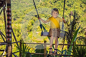 Young boy swinging in the jungle rainforest of Bali island, Indonesia. Swing in the tropics. Swings - trend of Bali