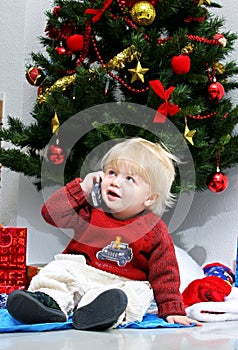Young boy talking on mobile phone under a christmas tree.