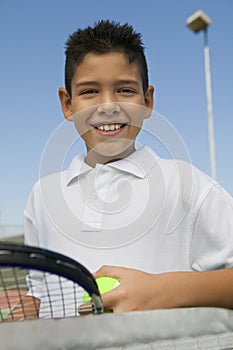 Young boy with tennis racket and ball at net on tennis court portrait close up