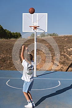 Young boy throwing ball into the hoop while playing basketball on an outdoor court.