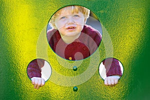 Young boy or toddler looking through holes in a wall in a playground