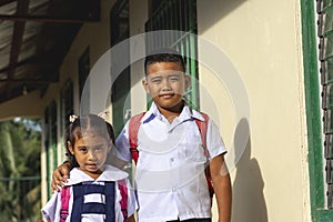 A young boy together with his younger sister outside the classroom.