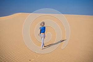 Young boy traveling in the desert. Sandy dunes and blue sky on sunny summer day. Travel, adventure, freedom concept