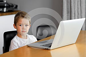 A young boy using a laptop computer sitting on top of a table at home