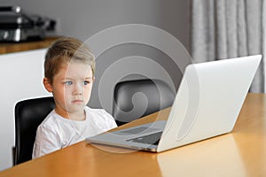 A young boy using a laptop computer sitting on top of a table at home