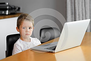 A young boy using a laptop computer sitting on top of a table at home