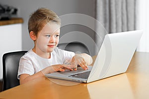 A young boy using a laptop computer sitting on top of a table at home