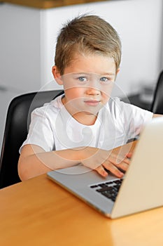 A young boy using a laptop computer sitting on top of a table at home