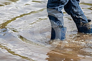 Young boy wading through mud of high tide with blue gumboots after a flood has broken the protecting dike