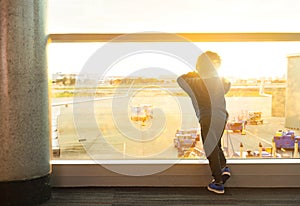 A young boy waiting to board a flight in an airport. Looking through the window at airplane departures