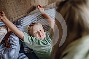 Young boy waking up in the morning for school. Mother helping son out of bed, preparing him for first day at school.