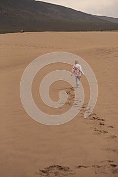 Young boy walking across sand dune with trail of footprints