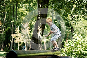 A young boy walks on a log at the playground. Active summer vacation