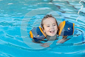 A young boy is in the water wearing flotation devices