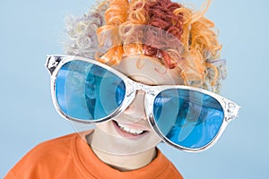 Young boy wearing clown wig and sunglasses smiling