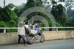 Young boy wearing jacket standing next to the motorcycle at the roadside bridge