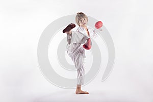 Young boy wearing kimono and red boxing gloves showing exercices