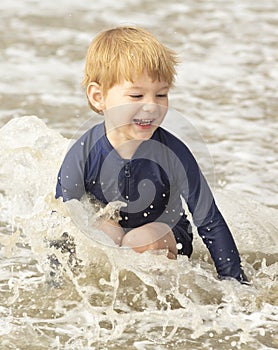 Young boy with blonde hair and navy swimsuit having fun splashing at the beach