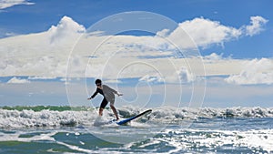 Young boy wearing swimming goggles stable stands on soft board while practicing surfing in beginner`s class