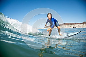 Young boy in a wetsuit surfing in the ocean.