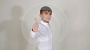 Young boy in white shirt shows thumb up standing on white background in Studio.