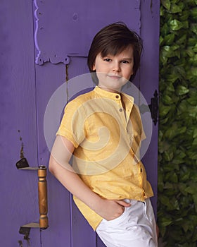 Young boy in a yellow shirt stands next to purple door. Studio shot. Concept of vacation and holidays