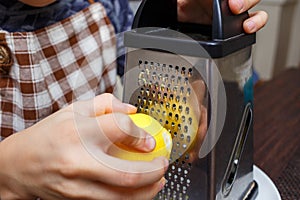 Young boy zesting lemon with grater at home kitchen