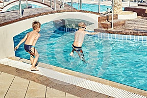 Young boys with bare torsos jumping into swimming pool