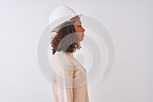 Young brazilian architect woman wearing security helmet over isolated white background looking to side, relax profile pose with