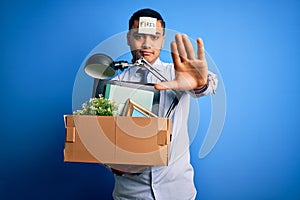 Young brazilian businessman holding box wearing reminder paper with fired message with open hand doing stop sign with serious and