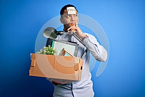 Young brazilian businessman holding box wearing reminder paper with fired message serious face thinking about question, very