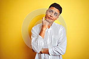 Young brazilian businessman wearing elegant shirt standing over isolated yellow background with hand on chin thinking about