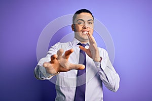 Young brazilian businessman wearing elegant tie standing over isolated purple background afraid and terrified with fear expression