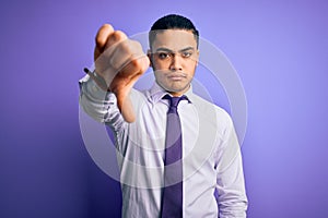 Young brazilian businessman wearing elegant tie standing over isolated purple background looking unhappy and angry showing