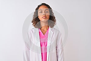 Young brazilian doctor woman wearing coat standing over isolated white background with serious expression on face