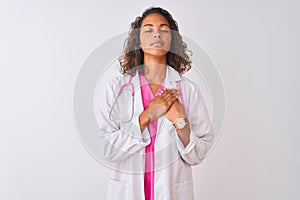 Young brazilian doctor woman wearing stethoscope standing over isolated white background smiling with hands on chest with closed