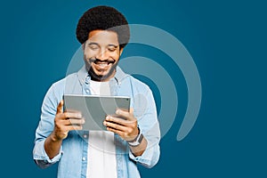 A young Brazilian man with an afro hairstyle is engrossed in his tablet, reading news or interacting with an application